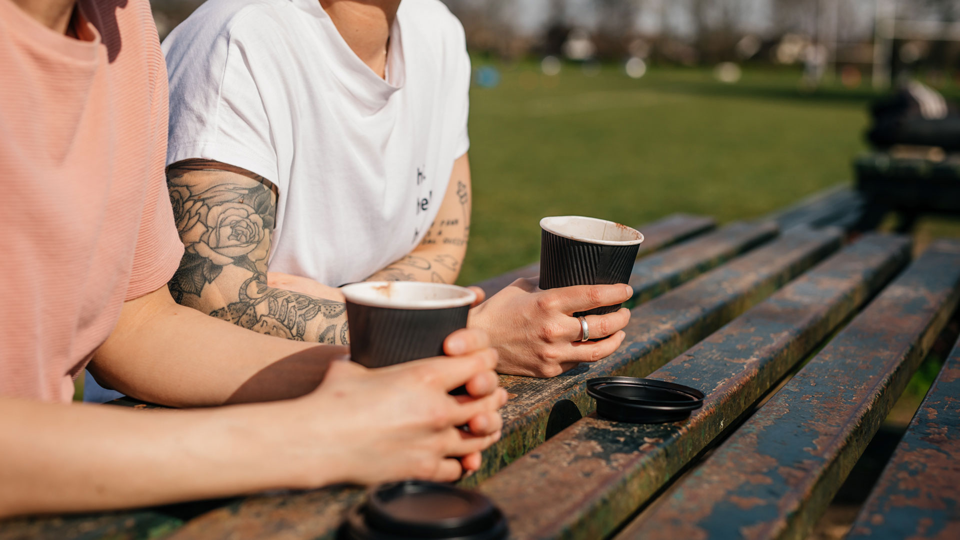 Two friends on a park bench drinking coffee