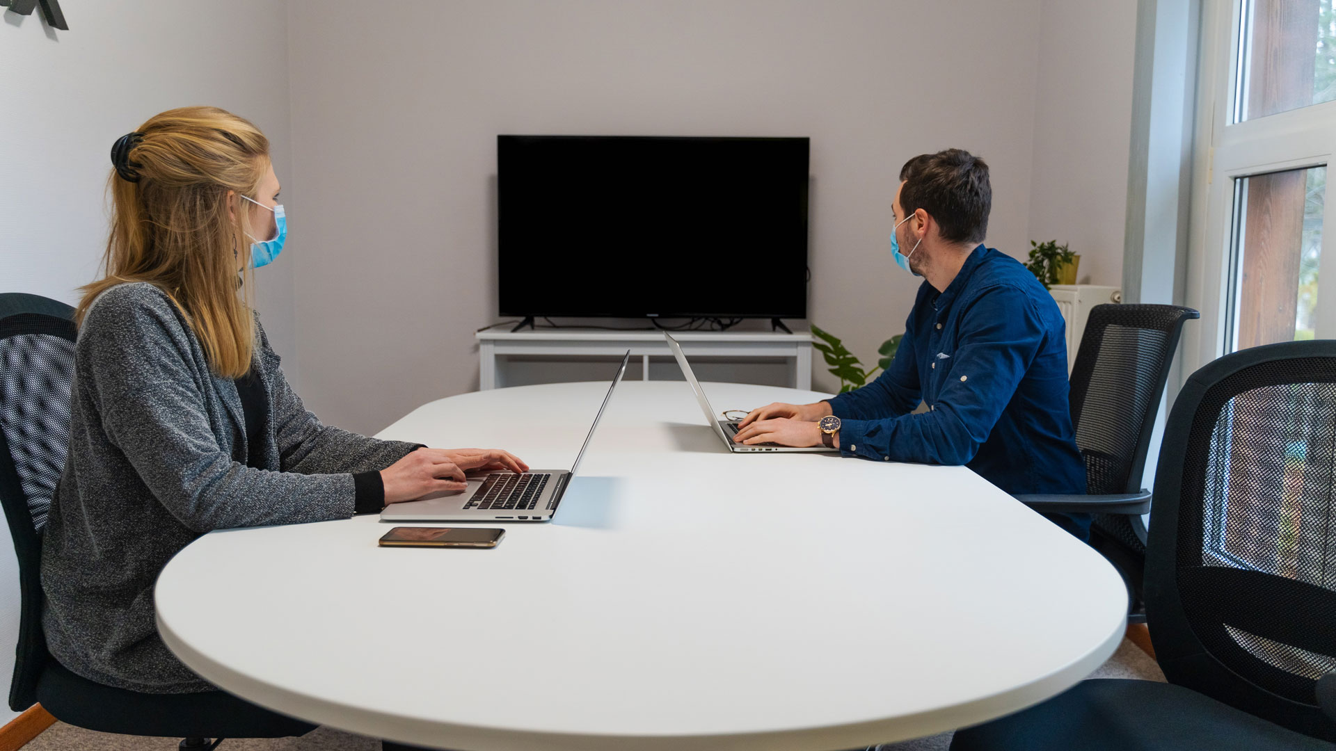 Two people wearing masks on their laptops